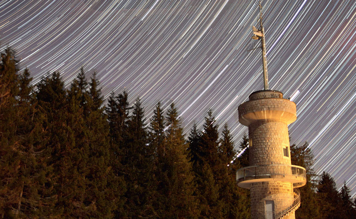 Deplasarea stelelor deasupra turnului de observație de pe Brend, un munte din sudul Pădurii Negre, cu înălțimea de 1149 de metri. Fotografia este alcătuită din 413 imagini a câte 15 secunde și arată astfel mișcarea stelelor pe parcursul a 100 de minute. Aparat de fotografiat: Canon 550D cu obiectiv de 20mm, apertură f/1.4. Deoarece o parte a turnului era luminată de un stâlp de iluminat aflat în fața unei pensiuni din apropiere, timpul de expunere al fiecărei fotografii a trebuit să țină cont de acest lucru pentru a evita ca partea respectivă a turnului să nu apară supraexpusă și arsă. U. Dittler